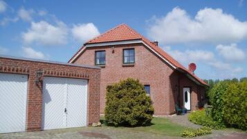 A two-story brick house with a red-tiled roof, a white garage door, and a small front yard with a bush.
