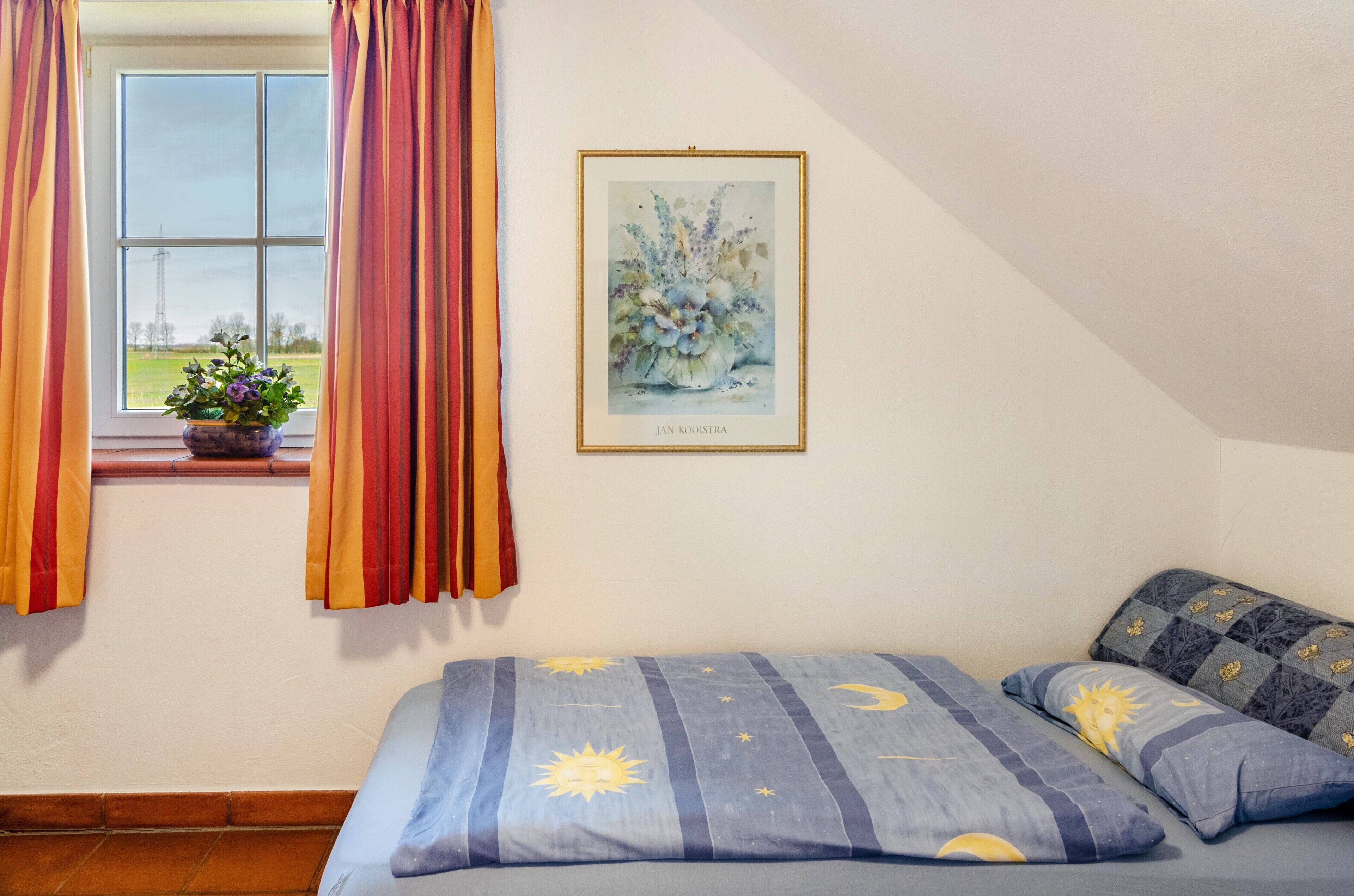 Une chambre à coucher avec un lit, une fenêtre avec des rideaux, un tableau encadré et une vue sur l’extérieur.
