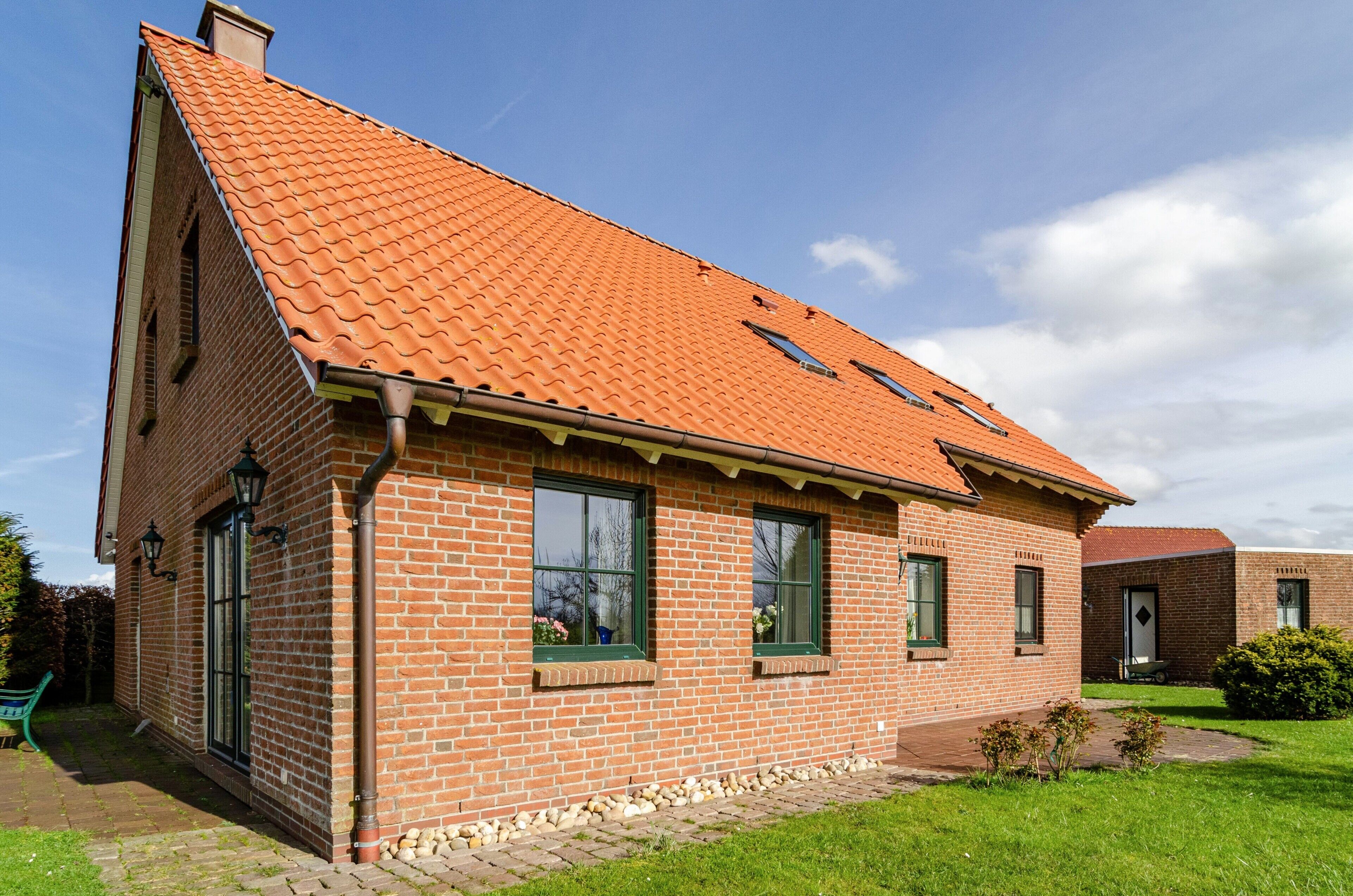 A brick house with a tiled roof, two windows with shutters, and a small garden area.