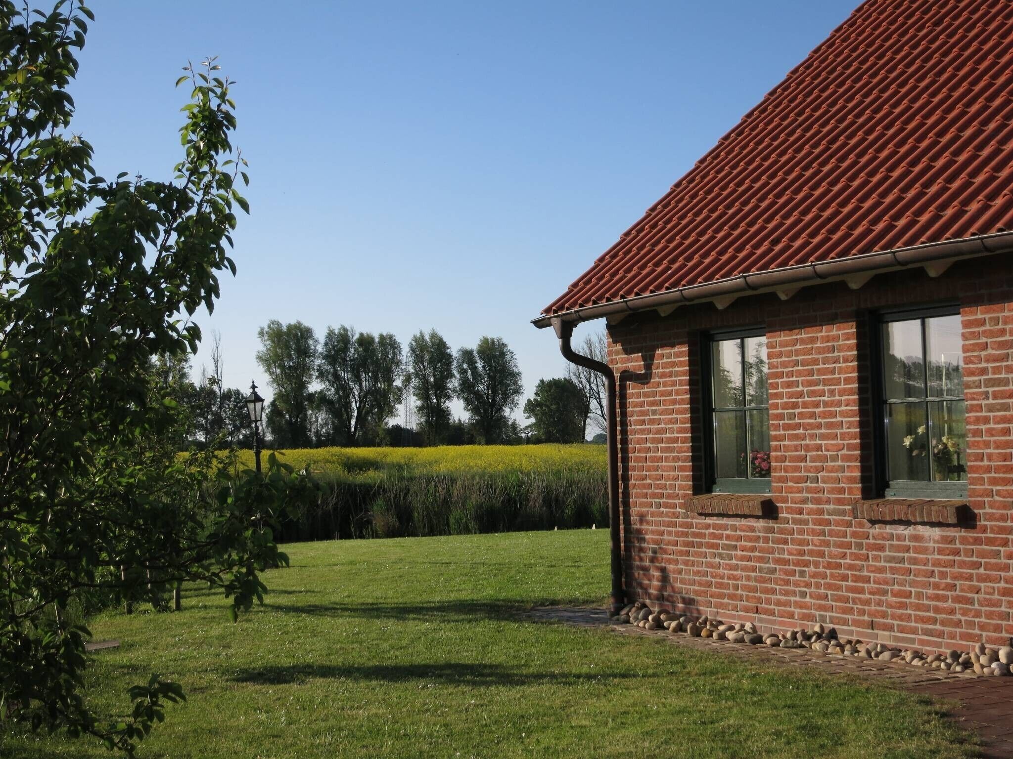 Een gebouw van baksteen met een dak van rode tegels, een gazon en bomen op de achtergrond.