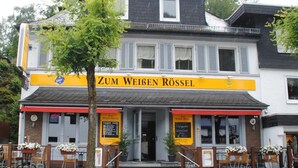 Un edificio con un letrero que dice 'Zum Weißen Rossel' y mesas y sillas para disfrutar al aire libre.