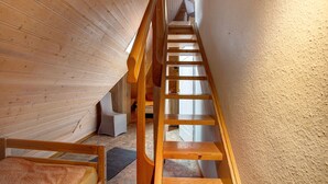 Una escalera de madera en una habitación con techo inclinado y una cama con colcha estampada.