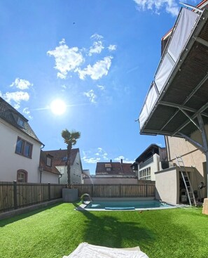 Un patio trasero con piscina, valla de madera y casas al fondo.