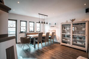 Un comedor con una mesa y sillas de madera, un armario con puertas de cristal y vistas a la ciudad a través de amplios ventanales.