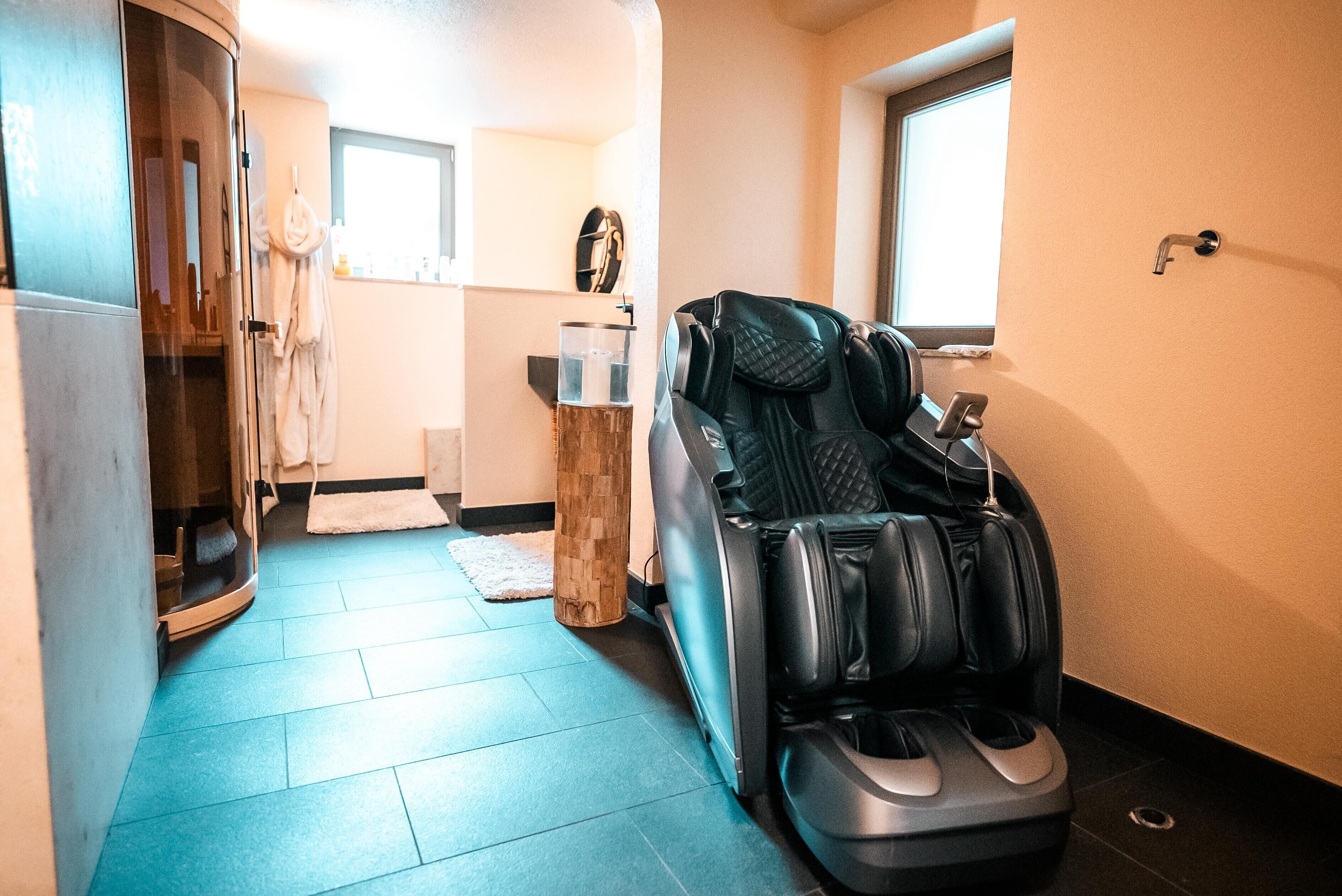 A massage chair in a room with a blue floor, a wooden stool, and a window.