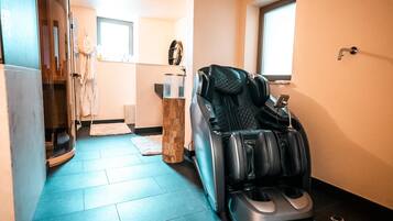 A massage chair in a room with a blue floor, a wooden stool, and a window.