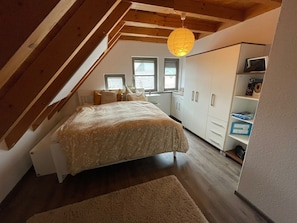 Un dormitorio con cama, escritorio, armario y ventana.