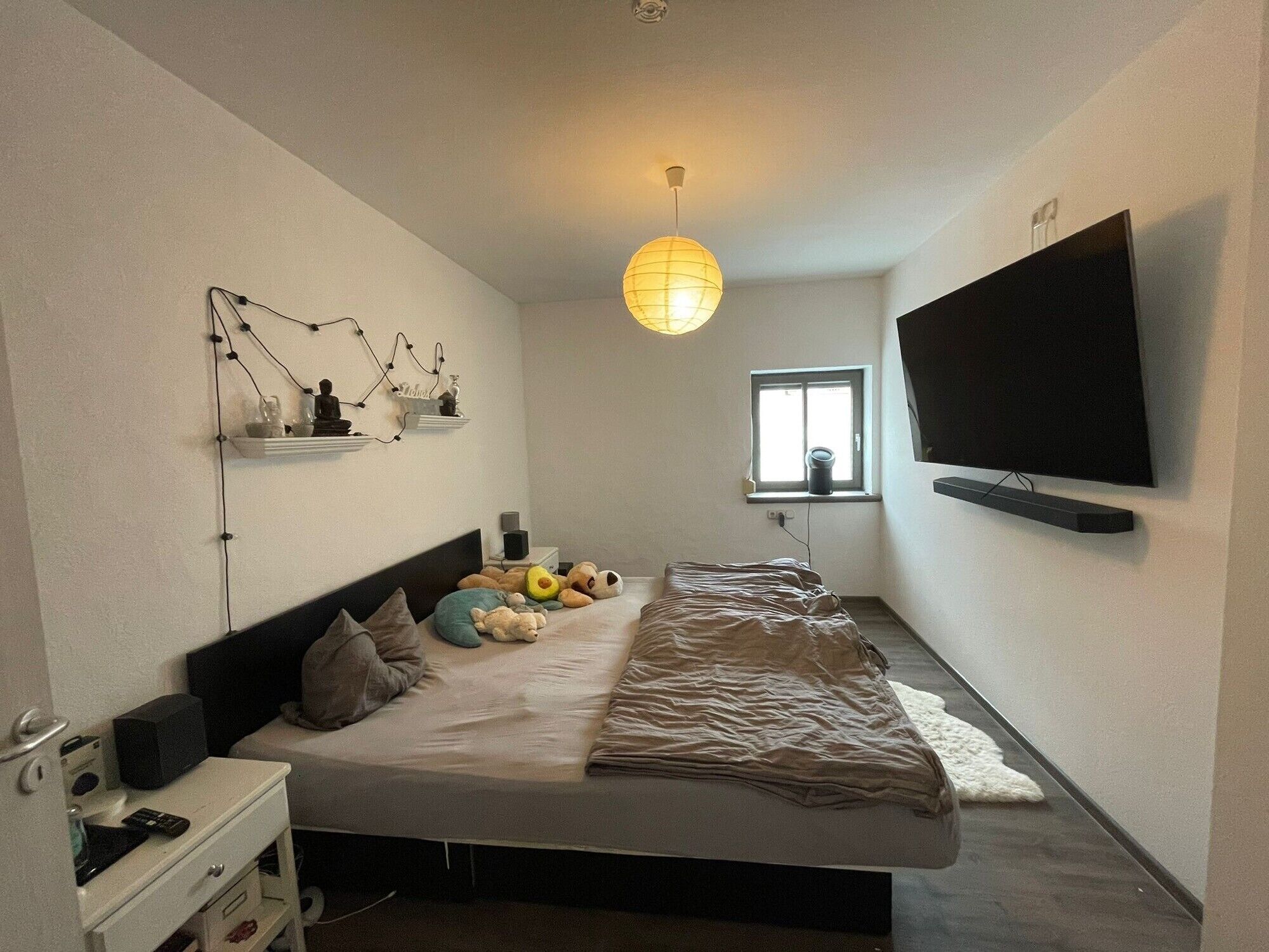 Ein Schlafzimmer mit einem Bett, einem Fernseher, einem Fenster und einer Wandablage mit Dekoration.