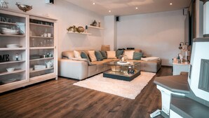 Een moderne woonkamer met een hoekbank, een glazen salontafel, een kast met servies en een open haard.