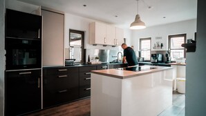 Een moderne keuken met een centraal eiland, zwarte keukenkastjes, en een persoon die kookt.