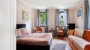 Ein Schlafzimmer mit einem Bett, einem Sofa, zwei Sesseln, einem Fernseher und einem kleinen Tisch mit einer Pflanze.