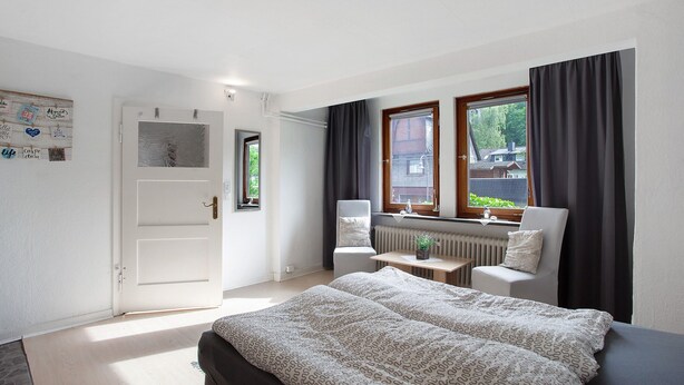 Une chambre à coucher avec un lit, deux chaises, une table, un radiateur et une fenêtre avec des rideaux.