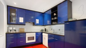 Une cuisine avec des meubles bleus, un lave-vaisselle blanc et un sol rouge.