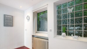Un couloir avec un radiateur, une horloge et une fenêtre décorée d’un motif de papillon.