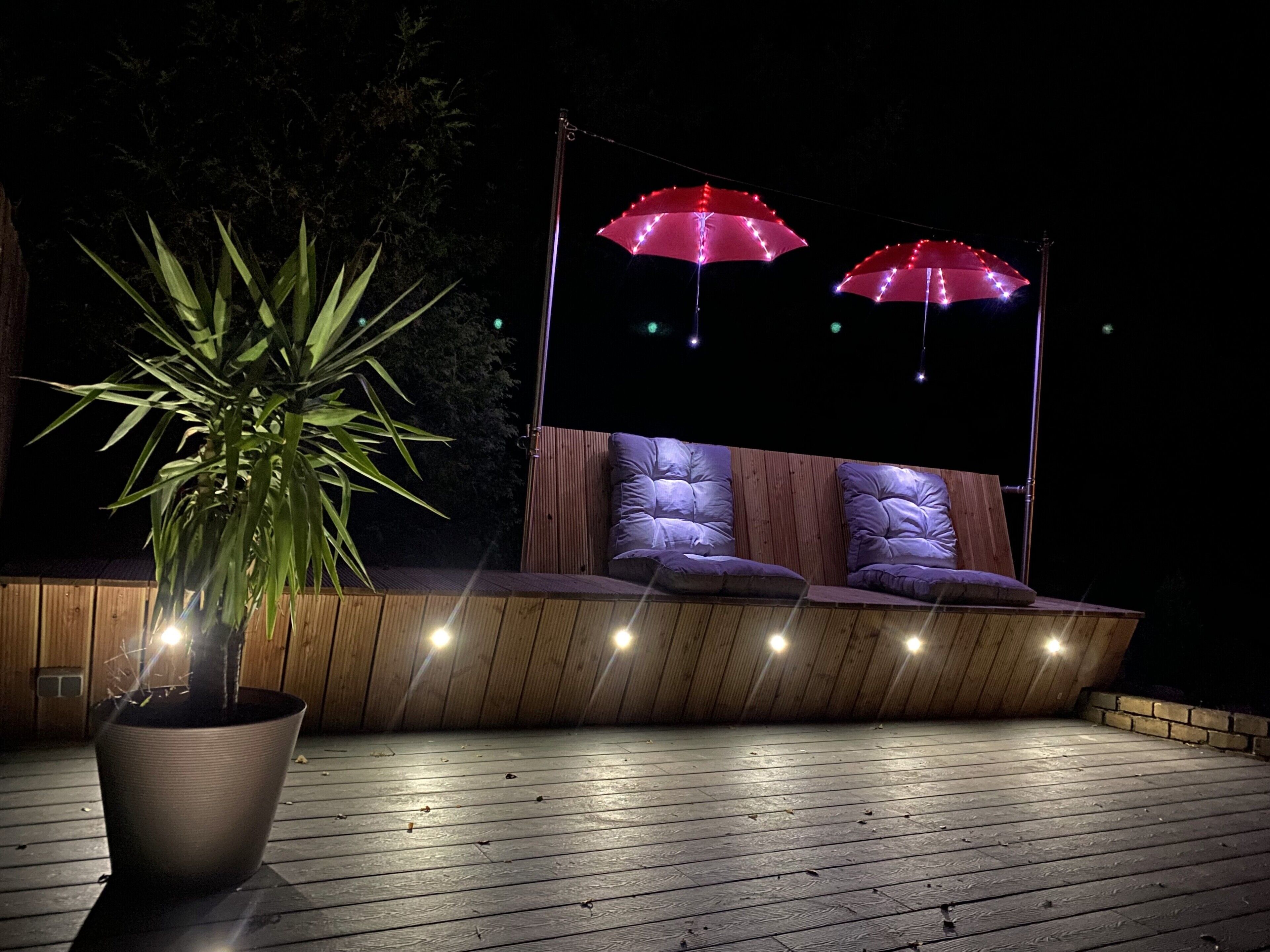 Een houten terras met een zithoek, voorzien van comfortabele banken en een plant in pot.
