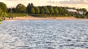 A waterfront view with a beach, trees, and a building with a sign that reads 'AMPHITHEATER.' - Holiday Home 'Ferienhaus' with Private Terrace, Shared Garden and Wi-Fi (Großkoschen)
