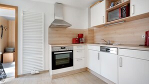 A modern kitchen with white cabinetry, a built-in oven, a coffee maker, and a microwave on a wooden shelf. - Holiday Home 'Ferienhaus' with Private Terrace, Shared Garden and Wi-Fi (Großkoschen)