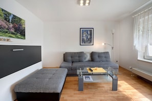 Un salon moderne avec un canapé, un pouf, une table basse en verre et des œuvres d’art accrochées aux murs.