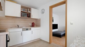 A modern kitchen with white cabinetry, a microwave, and a red kettle. There is a wooden floor and a visible bed in the adjacent room. - Holiday Home 'Ferienhaus' with Private Terrace, Shared Garden and Wi-Fi (Großkoschen)