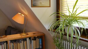 Une pièce avec une bibliothèque, une lampe, une plante en pot, un radiateur et un tableau encadré au mur.