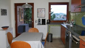 Une cuisine équipée d’une table à manger, de chaises, d’une machine à café, d’une bouilloire, avec vue sur l’extérieur par la fenêtre et un radiateur.