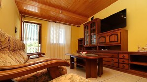 Un salón acogedor con techo de madera, un sofá, una mesa y un televisor sobre un mueble de madera.