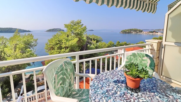 Un balcón con vista al mar, una planta en maceta y una mesa con cubierta de mosaico.
