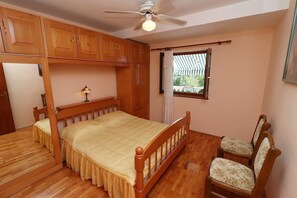 A bedroom with a wooden bed, a chair, a ceiling fan, and a window with curtains. - Seaside Apartments Markota (Blato)