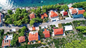 An aerial view of a coastal residential area with houses, a road, and a boat in the water. - Seaside Apartments Markota (Blato)
