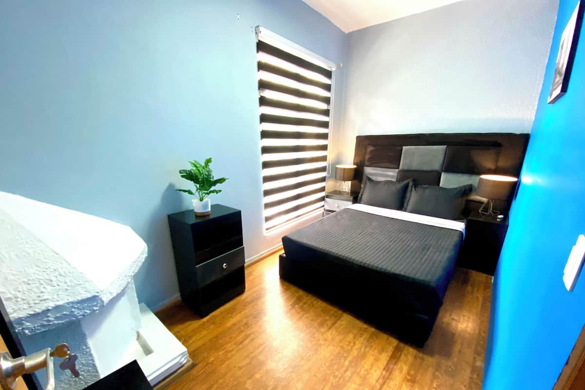 Een slaapkamer met een bed, nachtkastjes, een raam met jaloezieën en een deur.