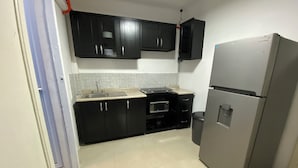 Een compacte keuken met donkere kastjes, een roestvrijstalen koelkast, een magnetron en een spoelbak.