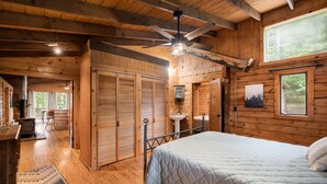 Ein Holzblockhaus-Interieur mit Bett, Deckenventilator, Spüle und Blick ins Freie.