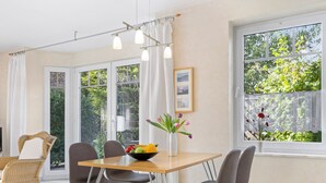 Ein Essbereich mit Tisch, Stühlen, einer Vase mit Blumen und Blick auf Grünfläche.