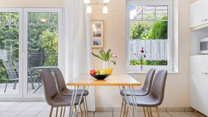 Eine moderne Küche mit Esstisch, Stühlen, einer Obstschale und Blick auf Grünflächen.