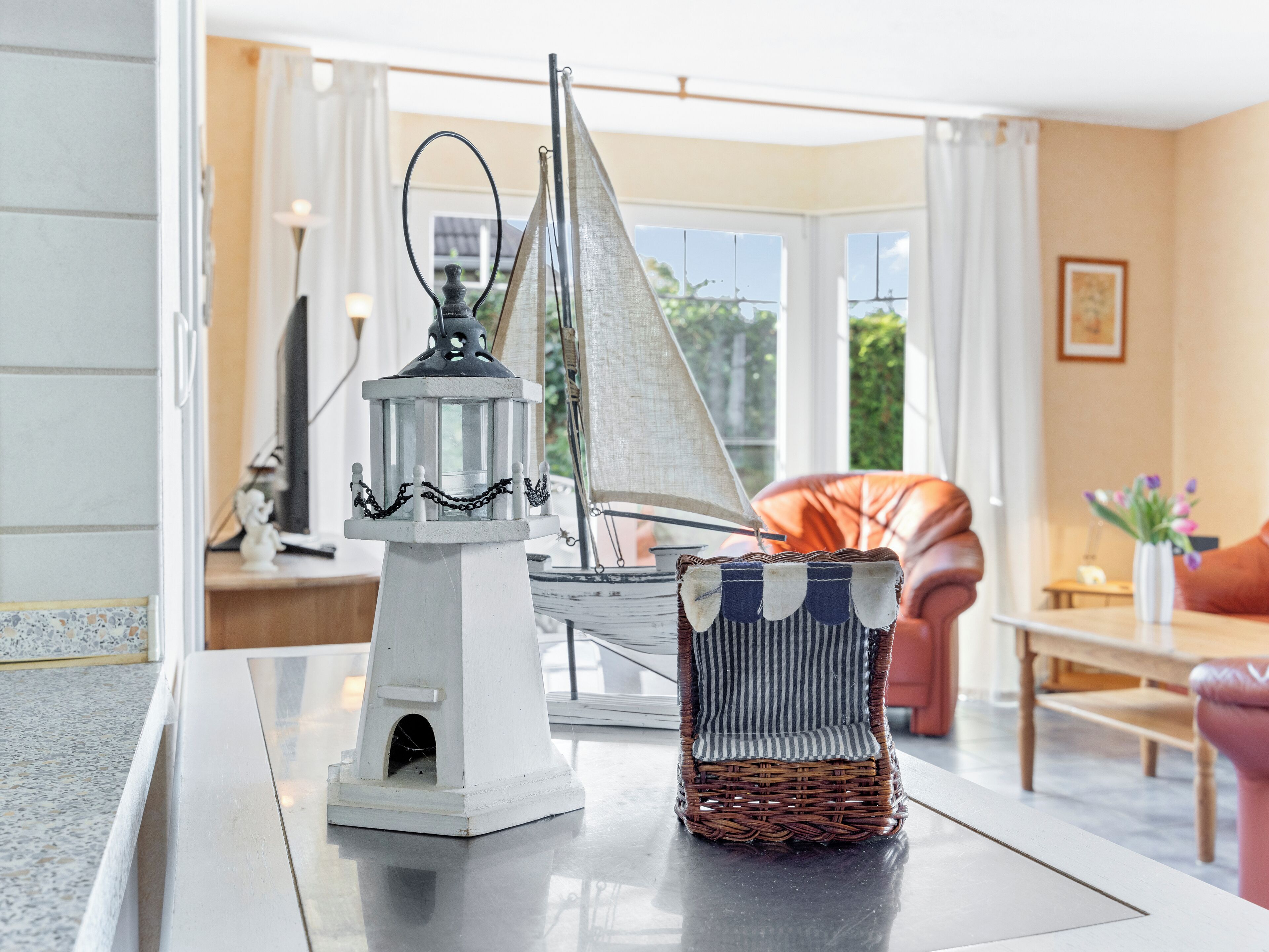A room with a white table, a wicker chair, a white lamp, and a sailboat model.
