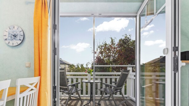 Un balcon avec une porte-fenêtre, deux chaises, une petite table et une horloge au mur.