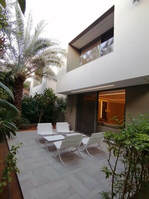 A modern outdoor patio with a dining area, surrounded by lush greenery and a building with large windows. - Vivienda Hada Residence (Riyadh)