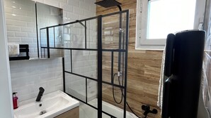 Een moderne badkamer met een douchecabine van glas, een witte wastafel en een houten opbergmeubel.