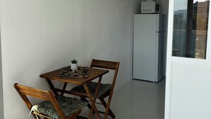Een klein zite hoek met een tafel en twee stoelen, een witte koelkast, en een airconditioner aan de muur.