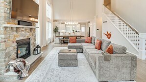 Un salon spacieux doté d’une cheminée, d’un grand canapé d’angle gris et d’un escalier menant à un autre niveau.