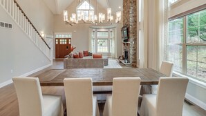 Un vaste salon doté d’une grande table à manger en bois, de sièges confortables, d’une cheminée et d’un escalier menant à un autre niveau.