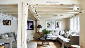 Un salon chaleureux avec un parquet en chevrons, un ensemble de canapés, une table basse et une lampe.