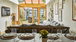 Un coin repas avec une table dressée pour quatre personnes, un canapé et une vue sur le jardin, visible à travers une porte vitrée.