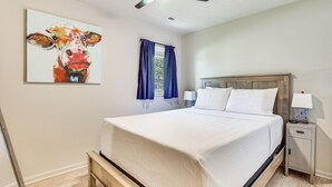 Una cama bien hecha con cabecera de madera, una mesita de noche con lámpara, y un cuadro de una vaca en la pared.