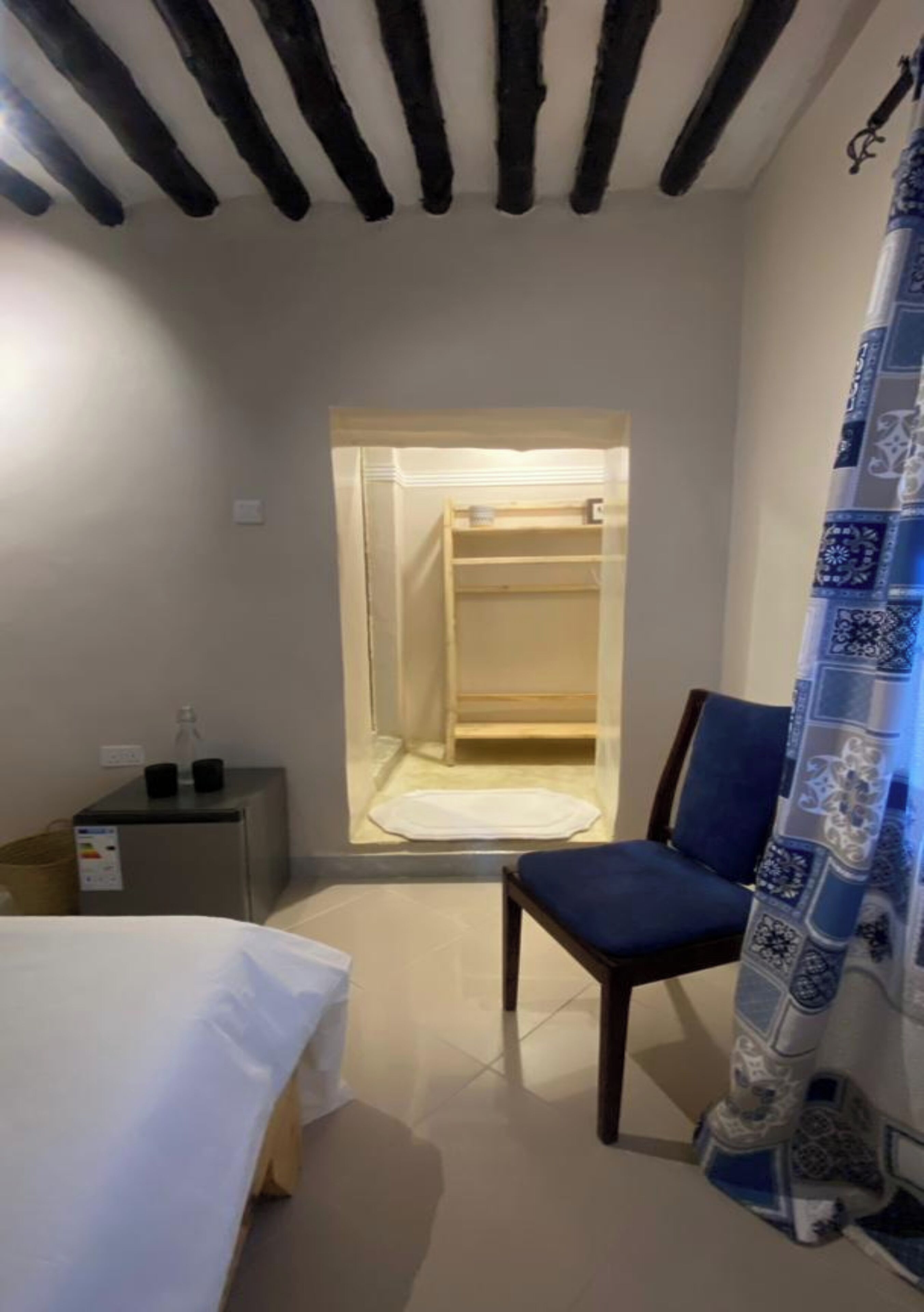 Een kleine kamer met een bed, een stoel, een bureau en een douche.