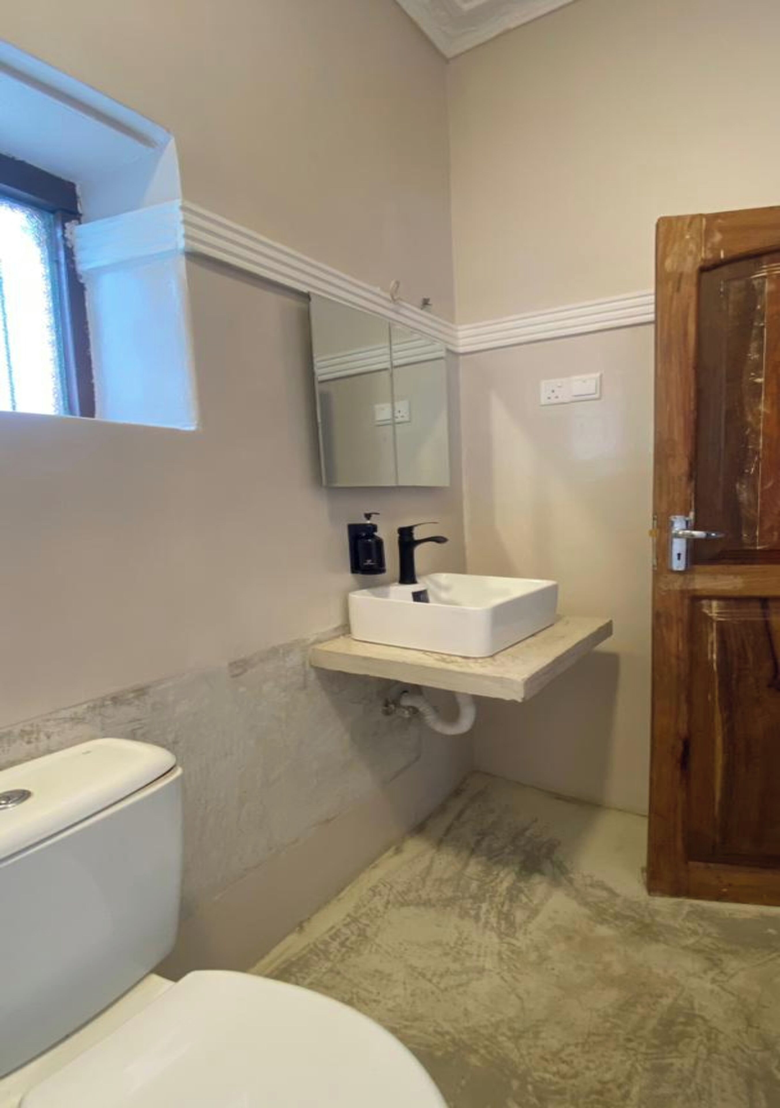 A small bathroom with a white toilet, a white sink with a mirror above it, and a wooden door.