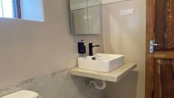 A small bathroom with a white toilet, a white sink with a mirror above it, and a wooden door.