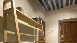 A wooden ladder shelf unit in a room with tiled flooring, a patterned ceiling, and a wooden door. - Hanaia House (Zanzibar Town)