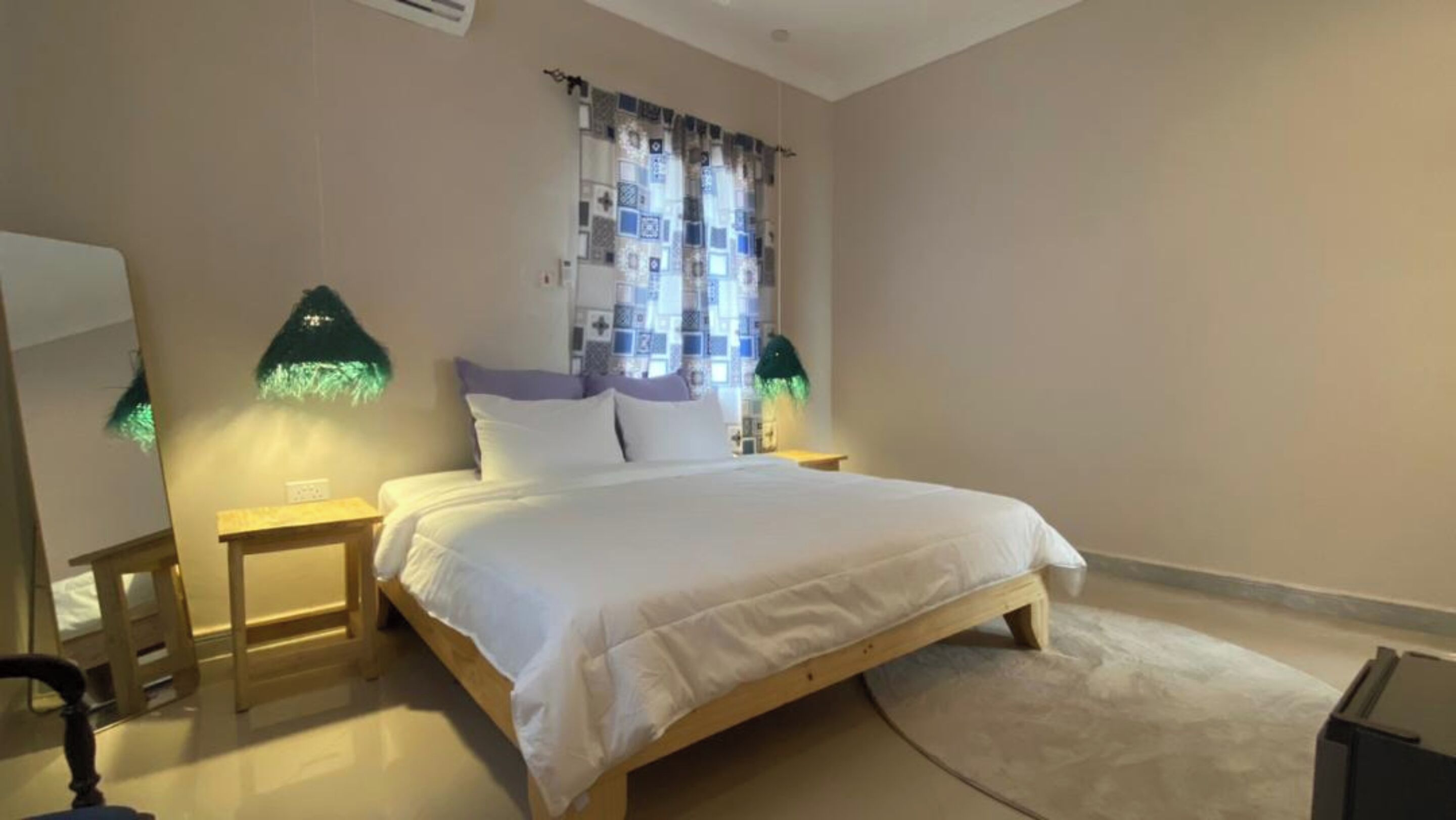 A bedroom with a wooden bed, a nightstand, a chair, and a large window with patterned curtains.