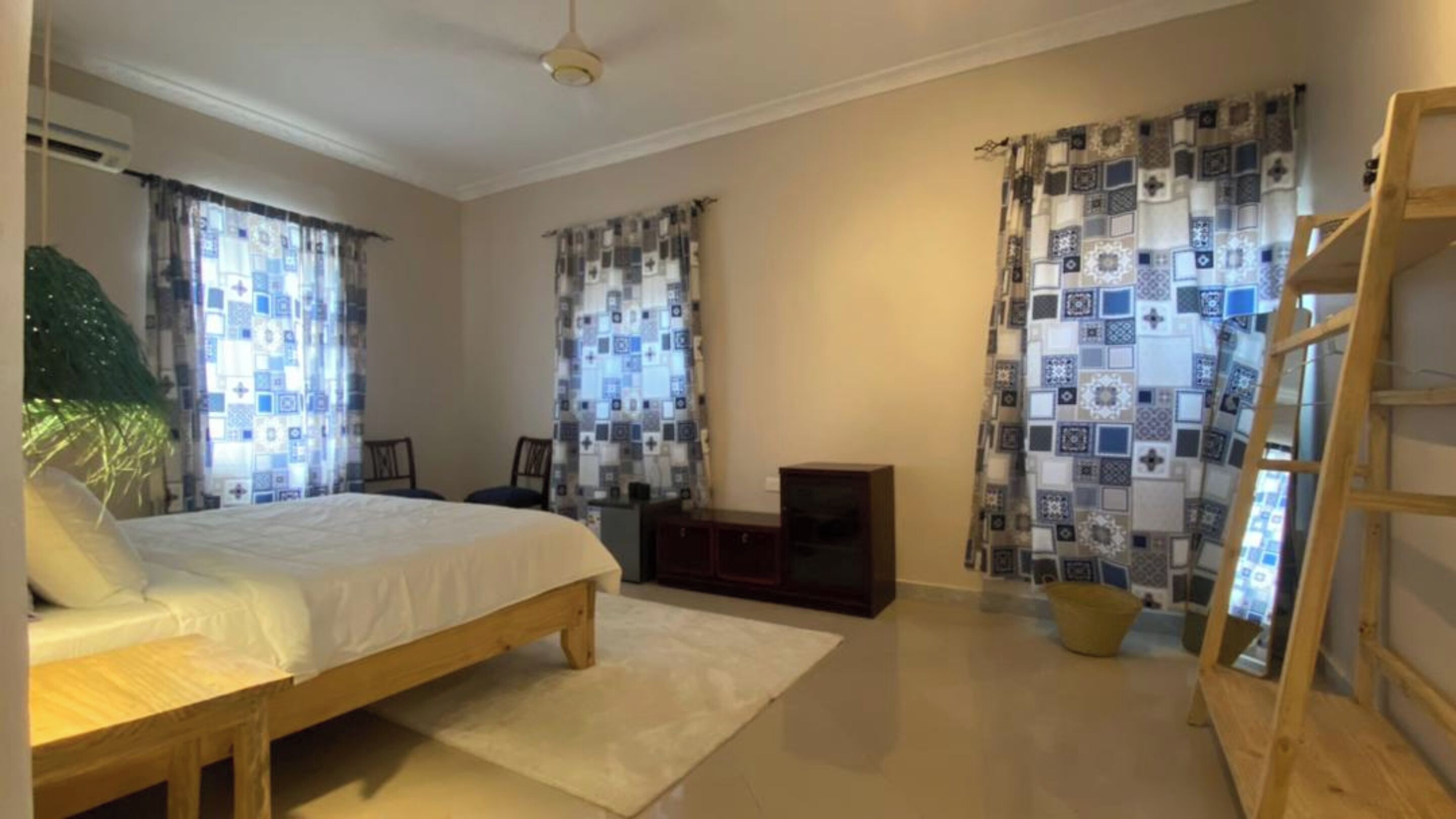 A bedroom with a bed, a TV, a wooden ladder, and patterned curtains.